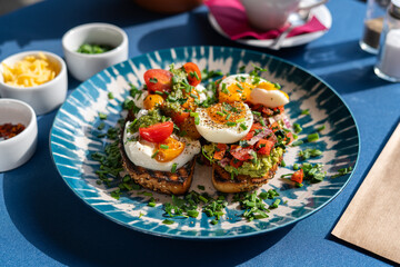 Soft-boiled eggs served with toast and pesto with avocado and red onion, served on a beautiful blue and white plate. A breakfast set illuminated by the morning sun.