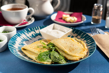 Pancakes with spinach and Greek yogurt served on a beautiful blue and white plate. A breakfast set illuminated by the morning sun.