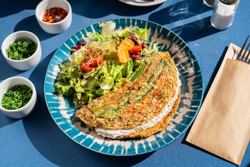 Omelette  with cottage cheese and fresh vegetables served on a beautiful blue and white plate. A breakfast set illuminated by the morning sun.