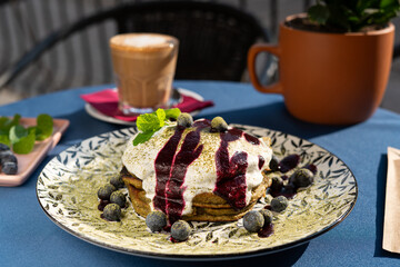 Fluffy matcha pancakes topped with juicy blueberries and velvety whipped cream, adorned with fresh mint leaves. Served on a white plate, glowing in morning sunlight – a vibrant, delicious breakfast  