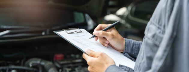 Auto check up and car service shop concept. Mechanic writing job checklist to clipboard to estimate repair quotation to client at workshop garage.