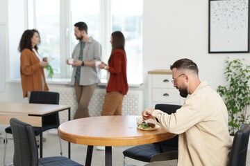 Fototapeta premium Man eating lunch at table. Colleagues having break in office