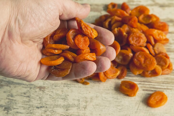 A hand holds a handful of dried apricots against a kitchen table background, dried apricots in hand.