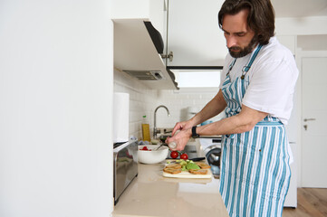 Man Preparing Vegan Salad in Modern Kitchen Wearing Striped Apron