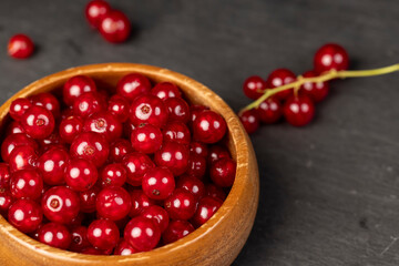 red currant poured in a wooden bowl, harvest small red currant berries on the kitchen table in a bowl, side view