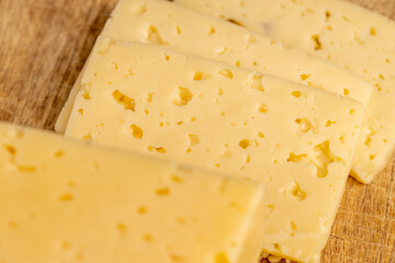 a piece of semi-hard cheese in place of slicing for cooking, pieces of sliced cheese on a cutting board, top view