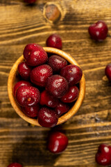 cherry in drops of water, wet red cherry fruits on the kitchen table closeup, berries in a wooden bowl