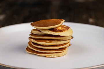 pancakes stacked together on a white bowl, side view, a tower of small milk pancakes on a ceramic bowl, close up