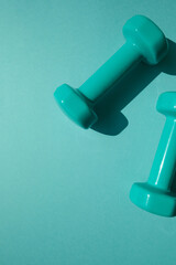 Sport or workout concept flat lay with blue dumbbells on the blue teal background. Copy space