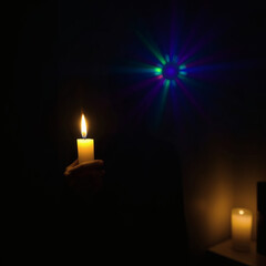 Person holding a candle with LGBT flag colors in a dim room