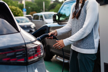 Charging an electric car in an urban setting. A modern woman engages with sustainable technology and green energy solutions for everyday mobility