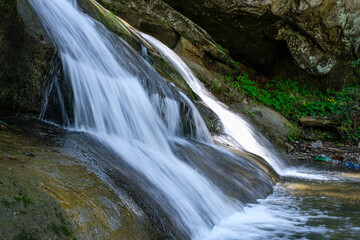Fototapeta premium Environmental issues near a beautiful waterfall with plastic bottles in the background. Long exposure to water. Carpathian Mountains, Ukraine. Copy space.