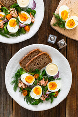 Salmon appetizer - cold smoked salmon, hard boiled eggs, leafy greens and mayonnaise with bread on wooden table	