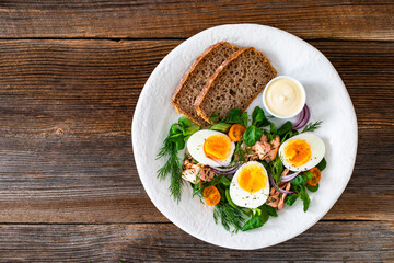 Salmon appetizer - cold smoked salmon, hard boiled eggs, leafy greens and mayonnaise with bread on wooden table	