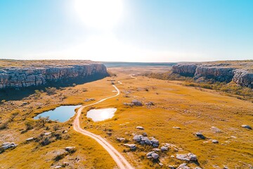 Scenic Aerial View of a Dirt Road Winding Through a Golden Grassland Valley with Rock Formations