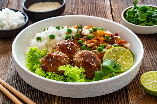Asian style fried meatballs with mixed vegetables served with white rice on wooden background