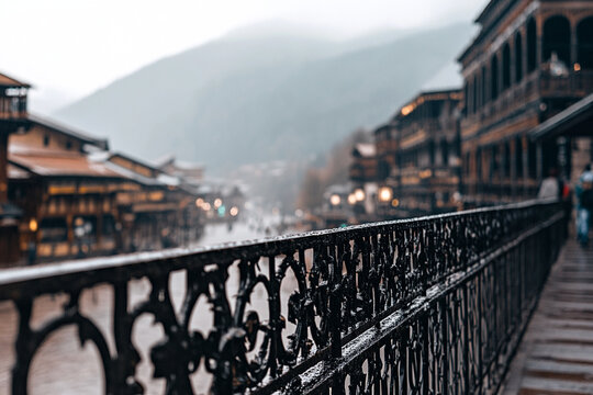 Close-up of ornate balcony railing overlooking a misty village in the mountains during a rainy day