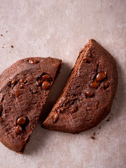 Broken Chocolate Cookie with Chips – Close-Up on Beige Stone Background. Rich texture and minimal style.