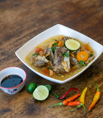 Traditional soup with meat and vegetables on wooden table with soy sauce, chili and lime on the side