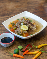 Vegetables soup with beef on white square plate on wooden table