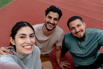 Three smiling athletes enjoying a selfie together on a vibrant running track, celebrating fitness,...