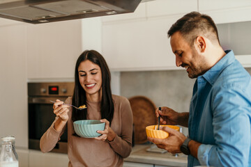 Happy couple eating breakfast cereal in modern kitchen