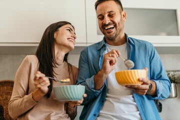 Happy couple enjoying breakfast and laughing together in kitchen