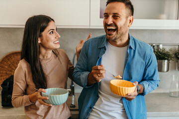Cheerful couple enjoying breakfast and laughing together in modern kitchen