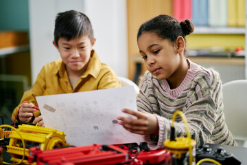 Children enthusiastically engaged in creative engineering projects, working on plans and models at classroom. Pencils, papers, and vibrant model components seen around children focusing on tasks