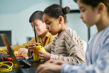 Group of children engrossed in STEM activities, using various gadgets and tools in classroom setting showing teamwork and concentration