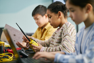 Group of children engaged in learning, using various technology and gadgets in classroom. Students concentrating on activities, with visible focus on a yellow device