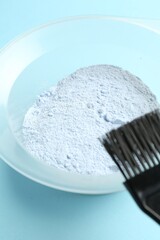 Bowl with hair bleaching powder and brush on light blue background, closeup