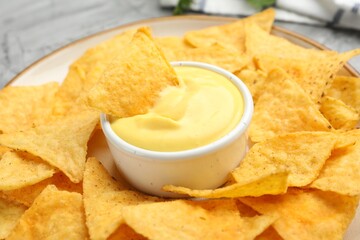 Tasty cheese dipping sauce in bowl and nacho chips on table, closeup