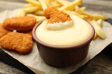 Delicious cheese sauce in bowl, chicken nuggets and French fries on table, closeup
