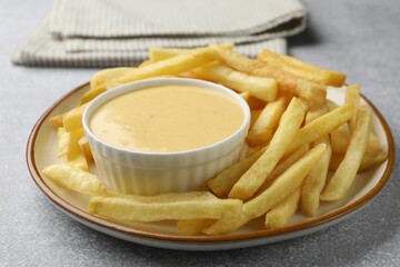 Tasty cheese sauce in bowl and French fries on grey table, closeup