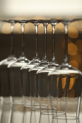 Upturned empty clean glasses on mirror surface against blurred background, closeup. Bokeh effect