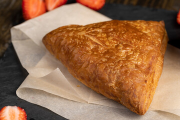 puff pastry with strawberries, a puff pastry bun with strawberry and cherry flavor lies on paper, closeup, top view