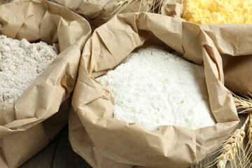Different types of flour in paper bags on wooden table, closeup