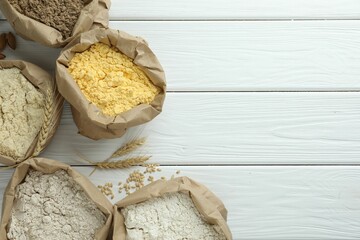 Different types of flour in paper bags on white wooden table, flat lay. Space for text