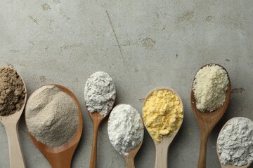 Different types of flour in spoons on light grey table, flat lay. Space for text