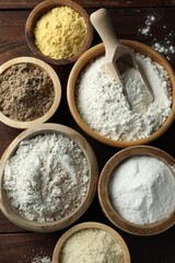 Different types of flour in bowls on wooden table, flat lay