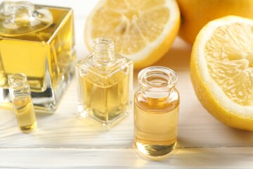 Open perfume bottles with aromatic essential oils and slices of lemons on white wooden table, closeup