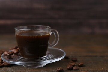 Aromatic coffee in glass cup and beans on wooden table, closeup. Space for text