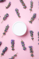 Flat lay of lavender flowers scattered around a white jar on a pink background, conveying relaxation and skincare concepts.