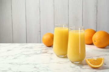 Orange juice in glasses and fresh fruits on white marble table, space for text