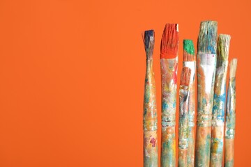Many dirty paintbrushes on orange background, closeup. Space for text