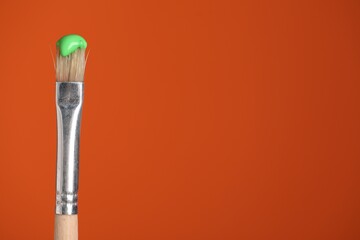 Brush with green paint on orange background, closeup. Space for text
