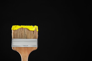 Brush with yellow paint on black background, closeup. Space for text