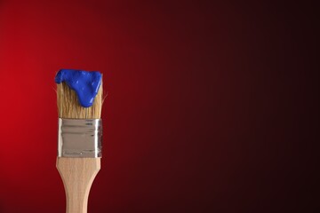 Brush with blue paint on red background, closeup. Space for text