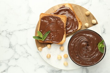 Tasty chocolate spread with mint and hazelnuts on white marble table, top view